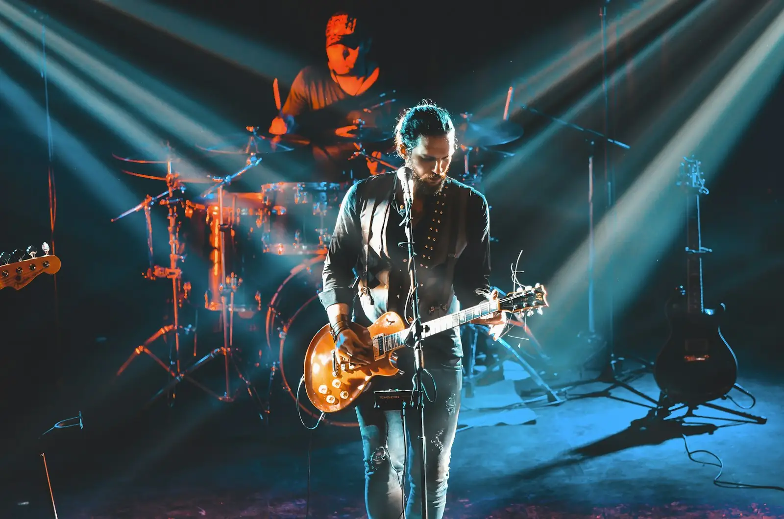 A guitarist and drummer playing under blue and amber stage light.